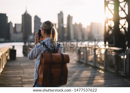 Back view of skilled amateur photographer taking pictures of American city enjoying summer trip to USA, female tourist with trendy rucksack testing modern technology for making view photos