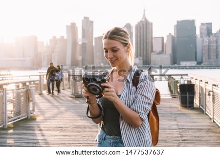 Happy woman tourist with old fashioned instant camera feeling good during time for exploring urban setting in America, successful young photographer editing pictures made with retro technology
