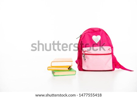 pink backpack with heart symbol and stack of books on white background with copy space