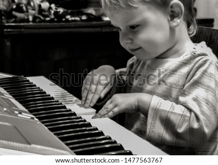 2010.10.03, Maloyaroslavets, Russia. Little blonde boy playing piano, side view, black and white photo.