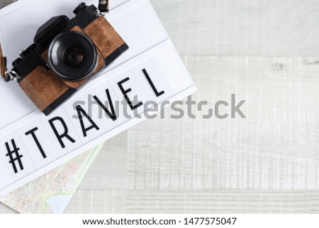 travel and photography concept - top view of camera, map and lightbox with hashtag travel over wooden table background