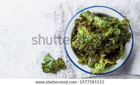 Green Kale Chips with salt on plate. Homemade healthy snack for low carb, keto, low calorie diet. Gray cement background. Ready-to-eat kale chips, copy space for text. Top view or flat lay. Banner Royalty-Free Stock Photo #1477581515