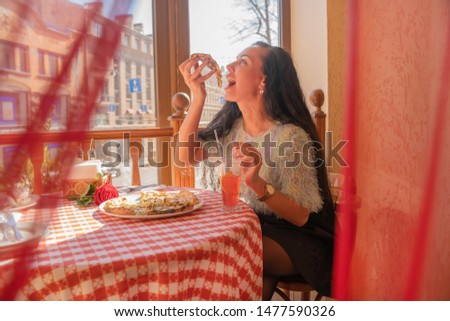 Funny brunette girl in sweater eating pizza at restaurant.