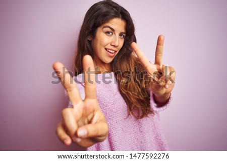 Young beautiful woman wearing sweater standing over pink isolated background smiling looking to the camera showing fingers doing victory sign. Number two.