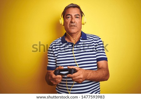 Middle age man playing video game using headphones over isolated yellow background with a confident expression on smart face thinking serious