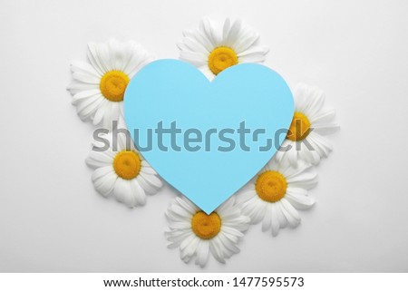 Beautiful chamomile flowers with empty heart shaped sheet of paper on white background, top view. Space for text