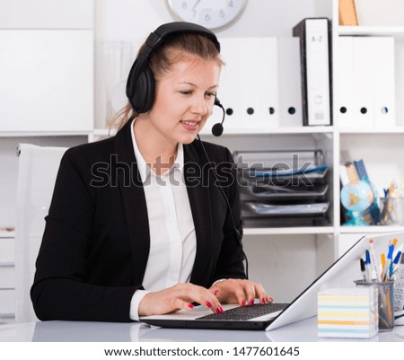 Young female in black suit is talking by headset with client in the office.