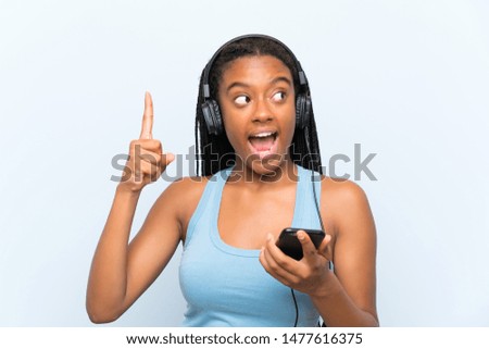 African American teenager girl with long braided hair listening music with a mobile intending to realizes the solution while lifting a finger up