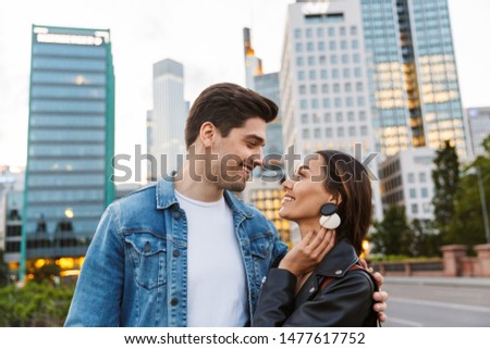 Image of smiling happy young loving couple hugging walking outdoors by street in city.