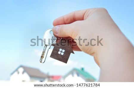 The mental key from door with wooden trinket in shape of house in woman's hand in front of sky