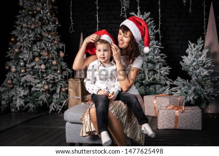 Christmas in the family: Mom and her son sit near the Christmas tree and try on Santas cap.