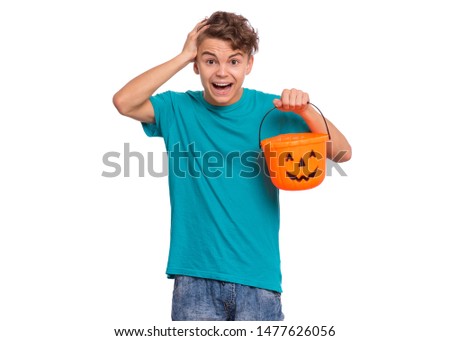 Happy halloween concept. Surprised or shocked teen boy holding orange pumpkin bucket, isolated on white background. Funny young teenager in amazement, touching head with hand. Child waiting candy.