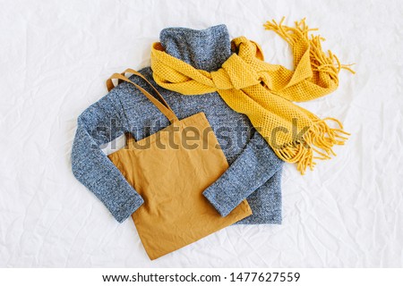 Blue sweater with yellow knitted scarf and tote bag. Autumn/winter fashion clothes collage on white background. Top view flat lay. 