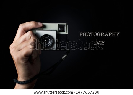 the hand of a man about to press the shutter button of a retro film camera, pointing to the observer, and the text photography day