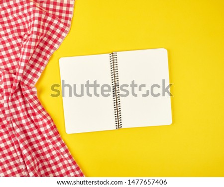 red textile napkin and open notebook, yellow background, top view, flat lay