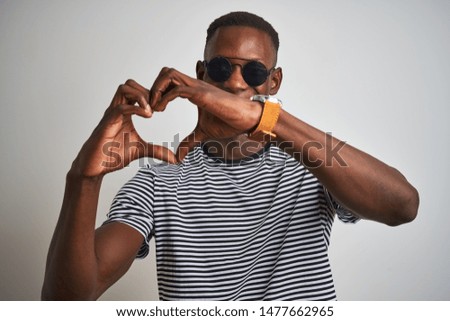 African american man wearing striped t-shirt and sunglasses over isolated white background smiling in love showing heart symbol and shape with hands. Romantic concept.