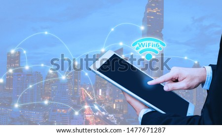 Wifi 6 internet network communication concept with double exposure of Young businessman standing and point to tablet and wifi icon with cityscape background.