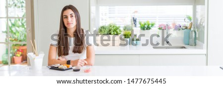 Wide angle picture of beautiful young woman eating asian sushi from delivery depressed and worry for distress, crying angry and afraid. Sad expression.