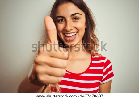 Young beautiful woman wearing red stripes t-shirt over white isolated background happy with big smile doing ok sign, thumb up with fingers, excellent sign