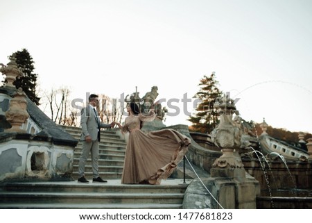 Loving couple together. Attractive young woman in dress and handsome man in suit are stand on the stairs  in Prague. The wind waves the dress. Celebrating.