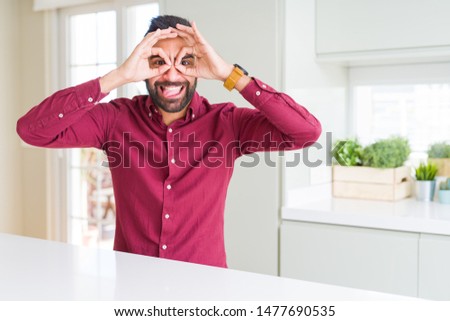 Handsome hispanic business man doing ok gesture like binoculars sticking tongue out, eyes looking through fingers. Crazy expression.