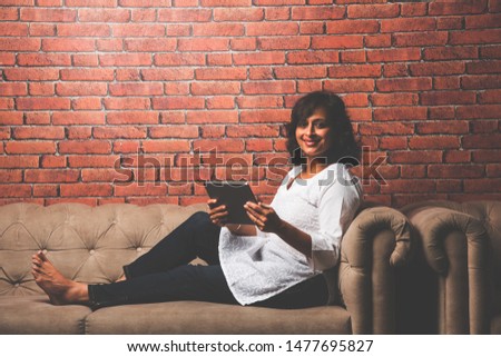 Indian Lady/women using Tablet PC while sitting on sofa/couch, selective focus