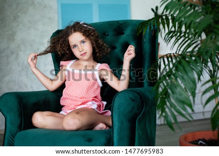 A little girl sits in a large armchair for adults. Velor, green, chic armchair.