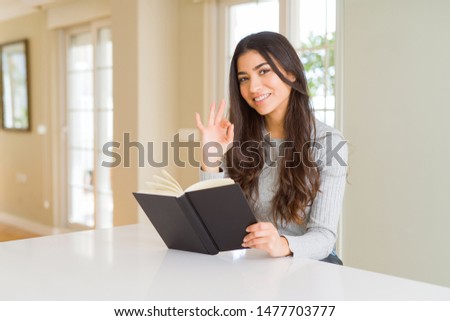 Young woman reading a book doing ok sign with fingers, excellent symbol