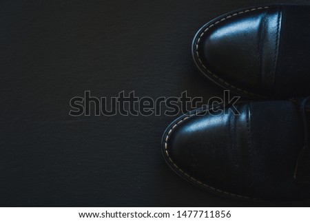 Black leather old man shoes on the right side on a dark background with copy space - Modern and fashionable pair of footwear for men on stone textured surface