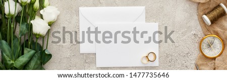 panoramic shot of golden rings on empty card, eustoma flowers, compass and bobbin on beige sackcloth on textured surface 