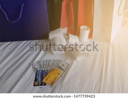 Credit cards and cash are spent to exchange for items in many colored paper bags with a slip and receipt, placed everything on white bed. Process with artificial instead of light from the window.