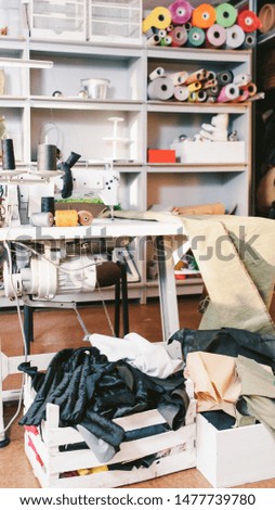 Mess in tailor studio. Seamstress workplace. Sewing machine, cloth rolls, thread spools, clothes in boxes.