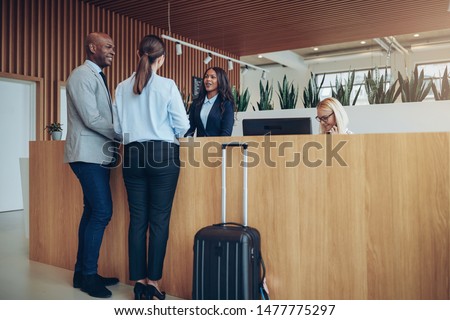 Two smiling guests talking with a concierge while checking in together at the reception counter of a hotel Royalty-Free Stock Photo #1477775297