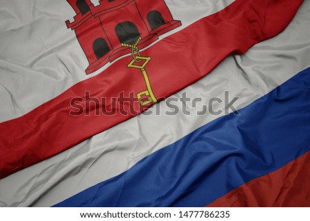 waving colorful flag of russia and national flag of gibraltar. macro
