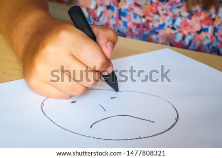 Little girl with black crayon draws sad face