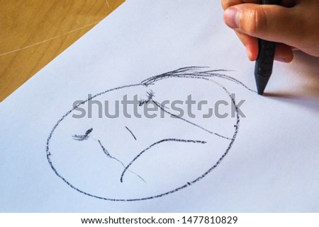 Child with a black crayon draws sad, crying face