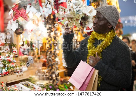 Cheerful African American looking for New Year decorations in traditional street market
