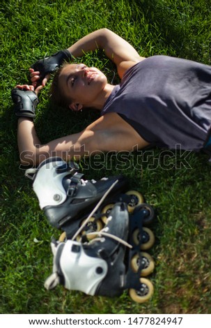 Young cheerful sport woman roller skater resting lying on the lawn grass in the park and listens to music with headphones