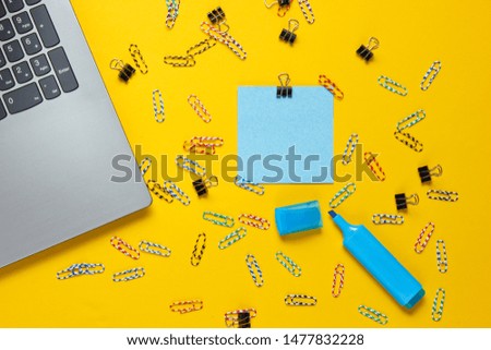 Minimalistic office still life. Laptop, stationery (paper clips, felt-tip pen, memo piece of paper) on yellow background. Studio shot. Top view