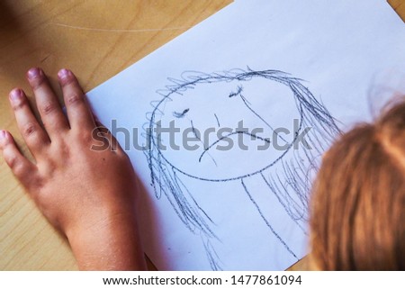 Little girl with a black crayon draws sad, crying face