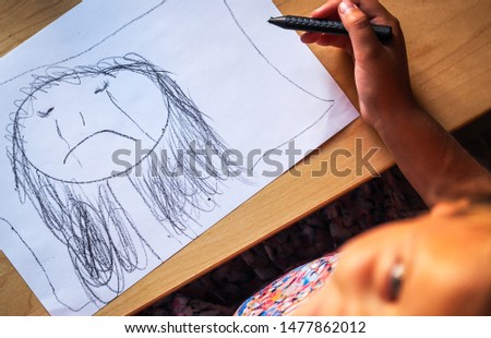 Little girl with a black crayon draw sad, crying face and happy looks in to the camera