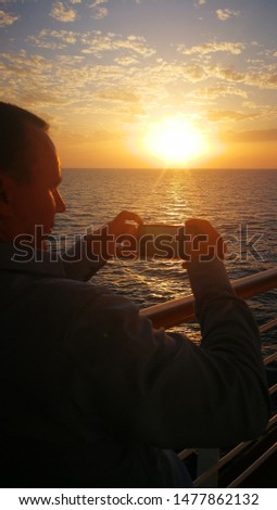 man removes the sunset on a cell phone from the deck of the ship.