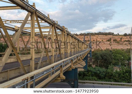 Angled view down large steel bridge crossing over river with mountain and cloudy skies