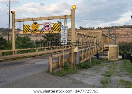 Large yellow steel girder bridge crossing river with mountainside in background with cloudy sky