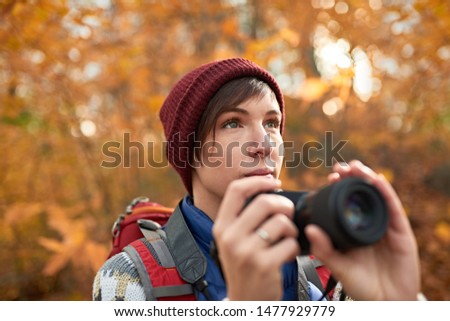 Attractive caucasian girl taking pictures with a mirrorless camera through the forest in the fall in Canada