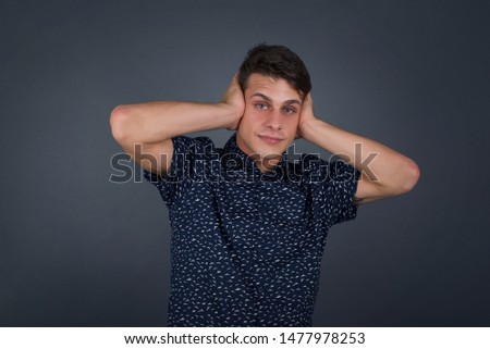 Man plugging ears with hands does not wanting to listen hard rock or loud music. European Young male ignoring noise or din covering his ears with hands avoiding loud sounds at street.