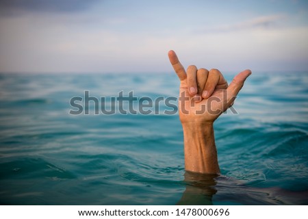 Hand of surfer making shaka (hang loose) sign in tropical blue waters