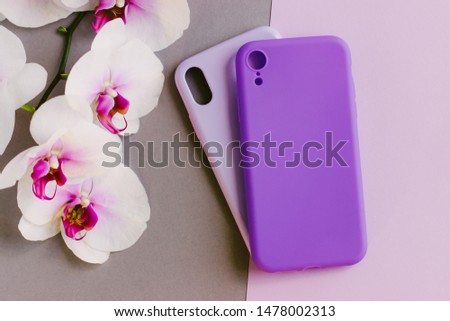 A branch of a beautiful Orchid and two silicone cases for your smartphone. Silicone mobile phone cases of lilac and purple colors lie on a pastel background. Selective focus.