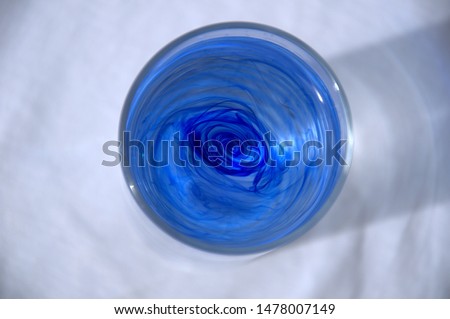 Stains of blue ink in water in a transparent glass on a white background