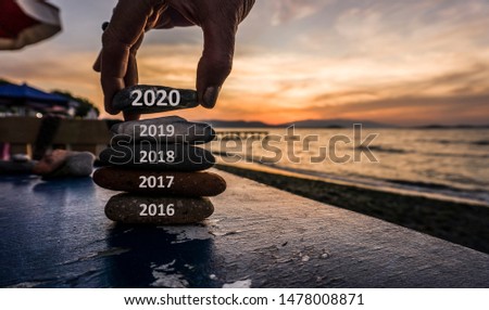 New Year 2020 is coming concept. Old year 2019 change to 2020 background. Turn of old year concept. Happy new year 2020 replace 2019. New hopes, excitement with 2020. Man adding stone to pebble tower. Royalty-Free Stock Photo #1478008871